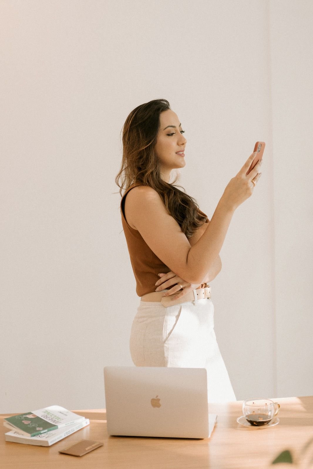 Kariny usando o celular ao lado de notebook e livros.